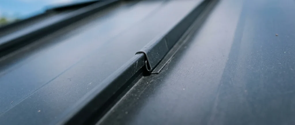Extreme close-up of two dark standing-seam metal roofing panels interlocking along an overlapping rib seam.